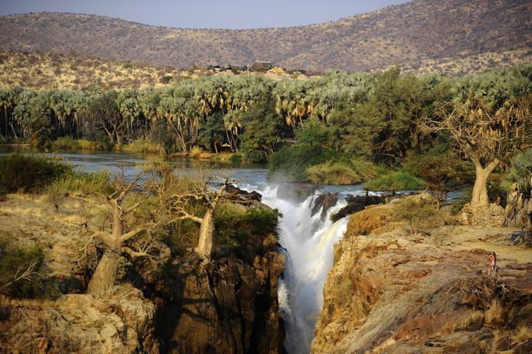 This picture taken on August 20, 2010 shows the Epupa Falls on the Kunene river, Northern Namibia, at the border with Angola.For generations Namibia's nomadic Himbas have buried their dead in the Baynes mountains along the Angolan border, where the Kunene River forms an oasis in the vast desert. Now the two nations are planning to build a 1,700-gigawatt hydroelectric dam which will flood some of the valleys and submerge gravesites, an act the Himbas fear will anger their ancestors who play a central role in their daily lives. AFP PHOTO / STEPHANE DE SAKUTIN