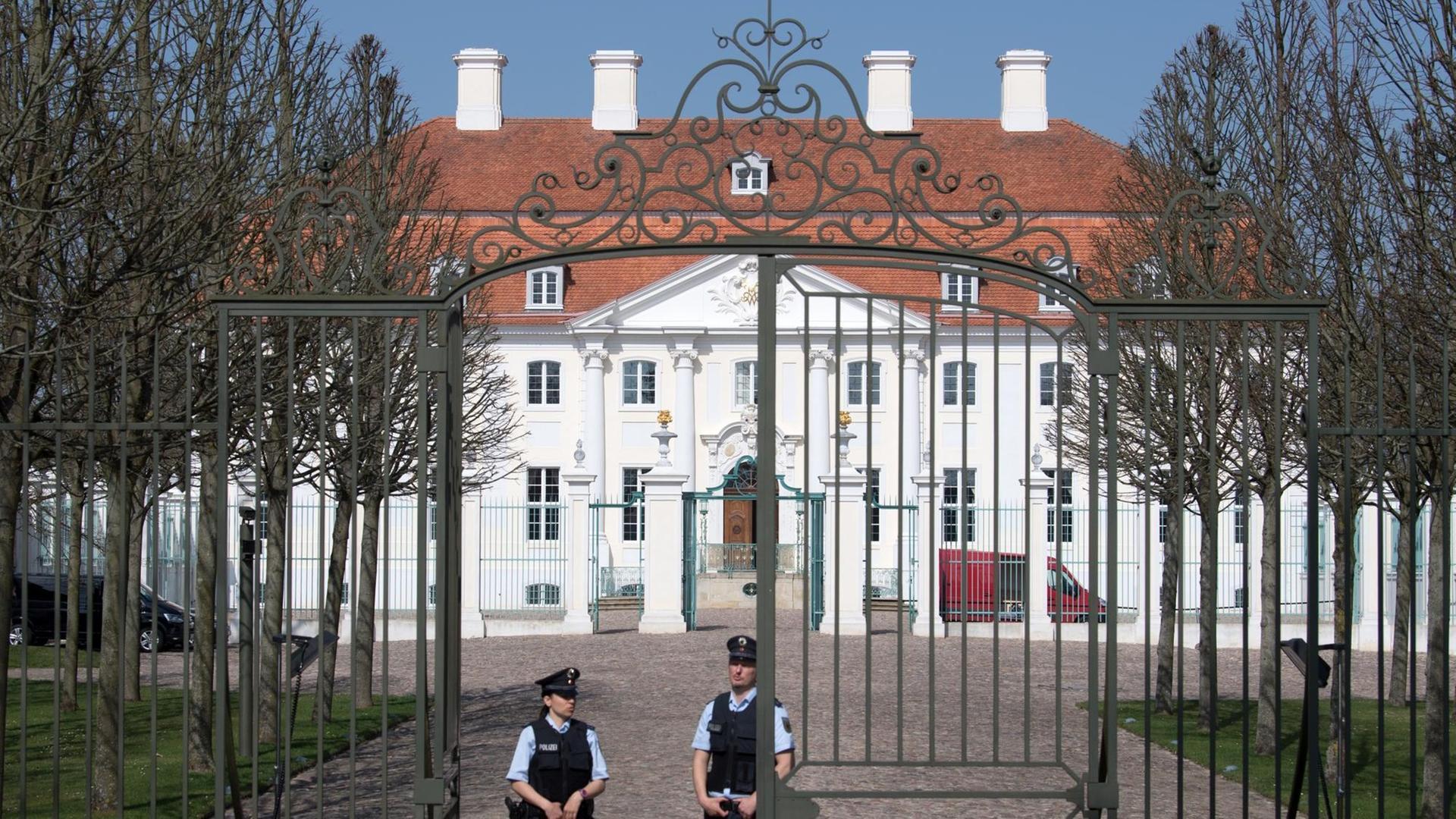 Im Hintergrund das Gästehaus, davor ein schmiedeeisernes Tor, das von zwei Polizisten bewacht wird.