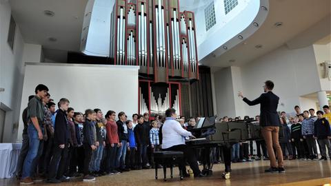 Der Knabenchor steht im Halbkreis auf einer Bühne um einen Flügel herum.