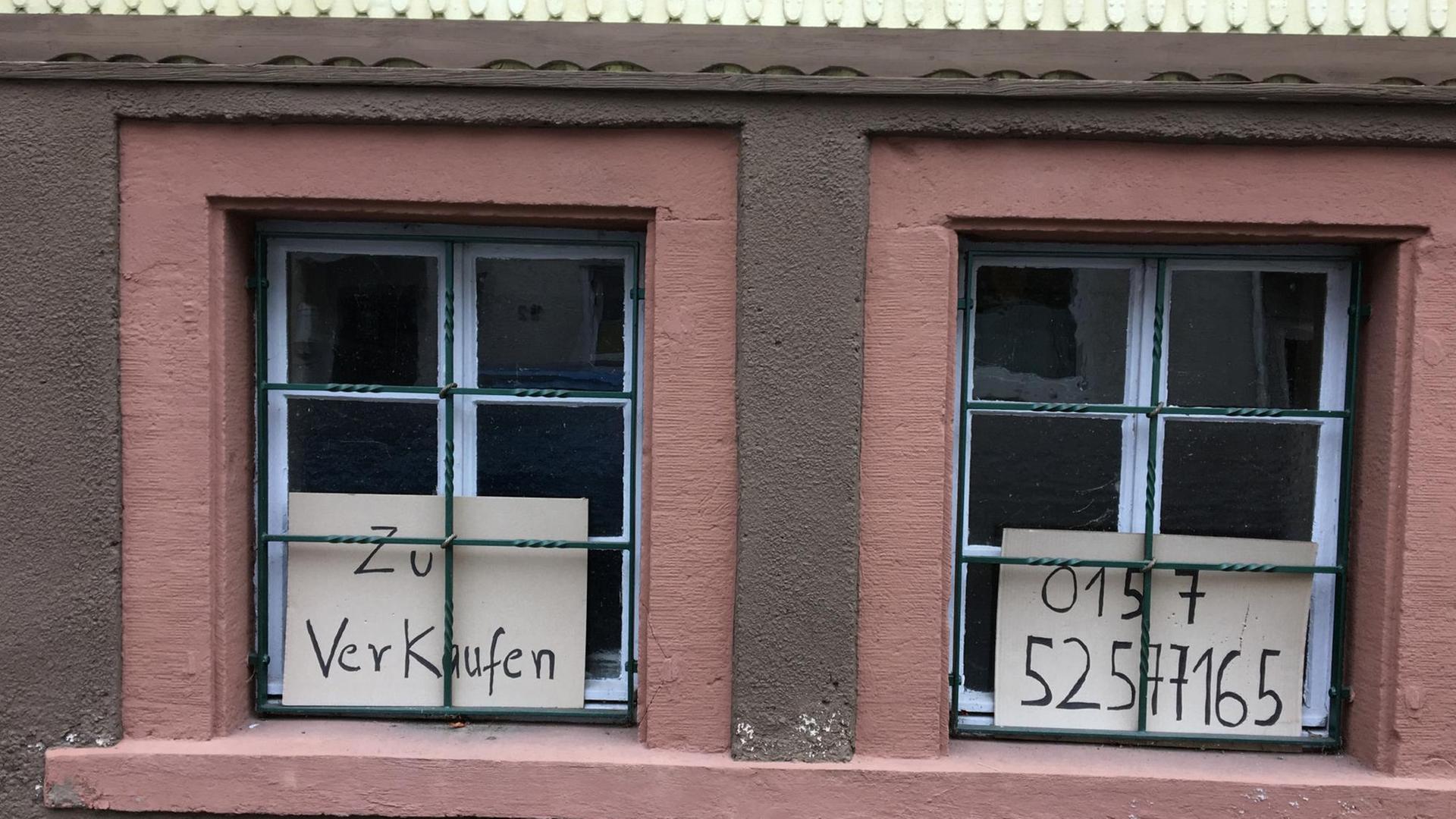 Zwei Fenster eines Hauses in Beerfelden, in dem Schilder zu sehen sind mit der Aufschrift "zu verkaufen" sowie einer Telefonnummer