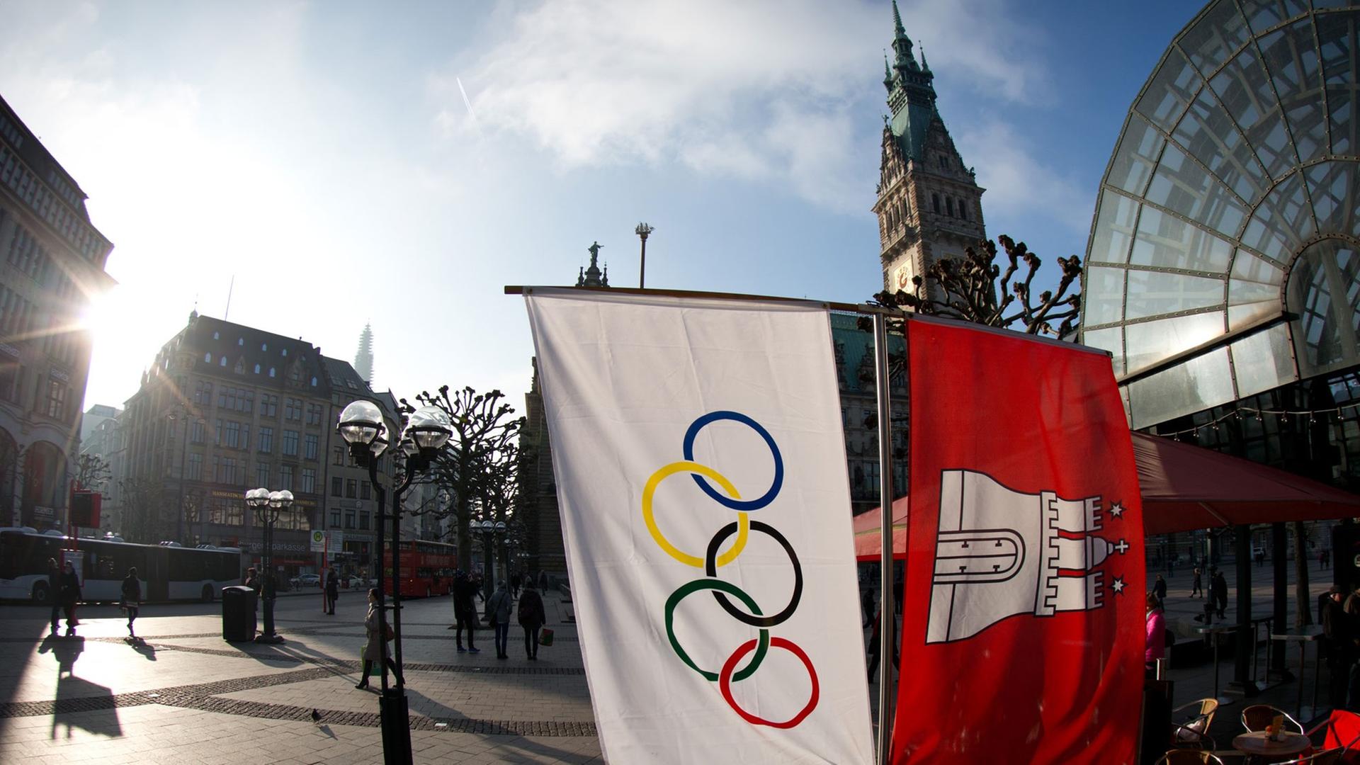 Flaggen mit den Olympischen Ringen und dem Wappen von Hamburg hängen neben einem Straßencafe am Rathausmarkt in Hamburg