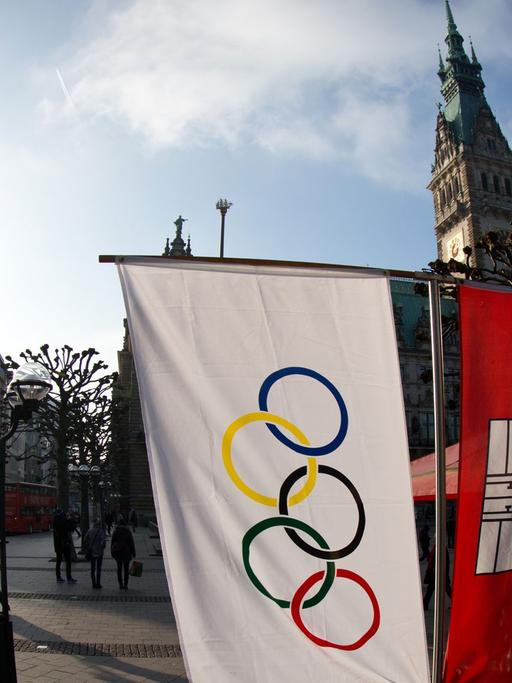 Flaggen mit den Olympischen Ringen und dem Wappen von Hamburg hängen neben einem Straßencafe am Rathausmarkt in Hamburg