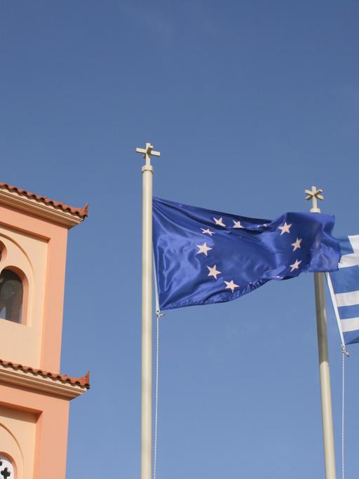 Europäische und griechische Flagge vor dem Kirchturm im Bergdorf Pano Hersonissos auf der griechischen Insel Kreta.