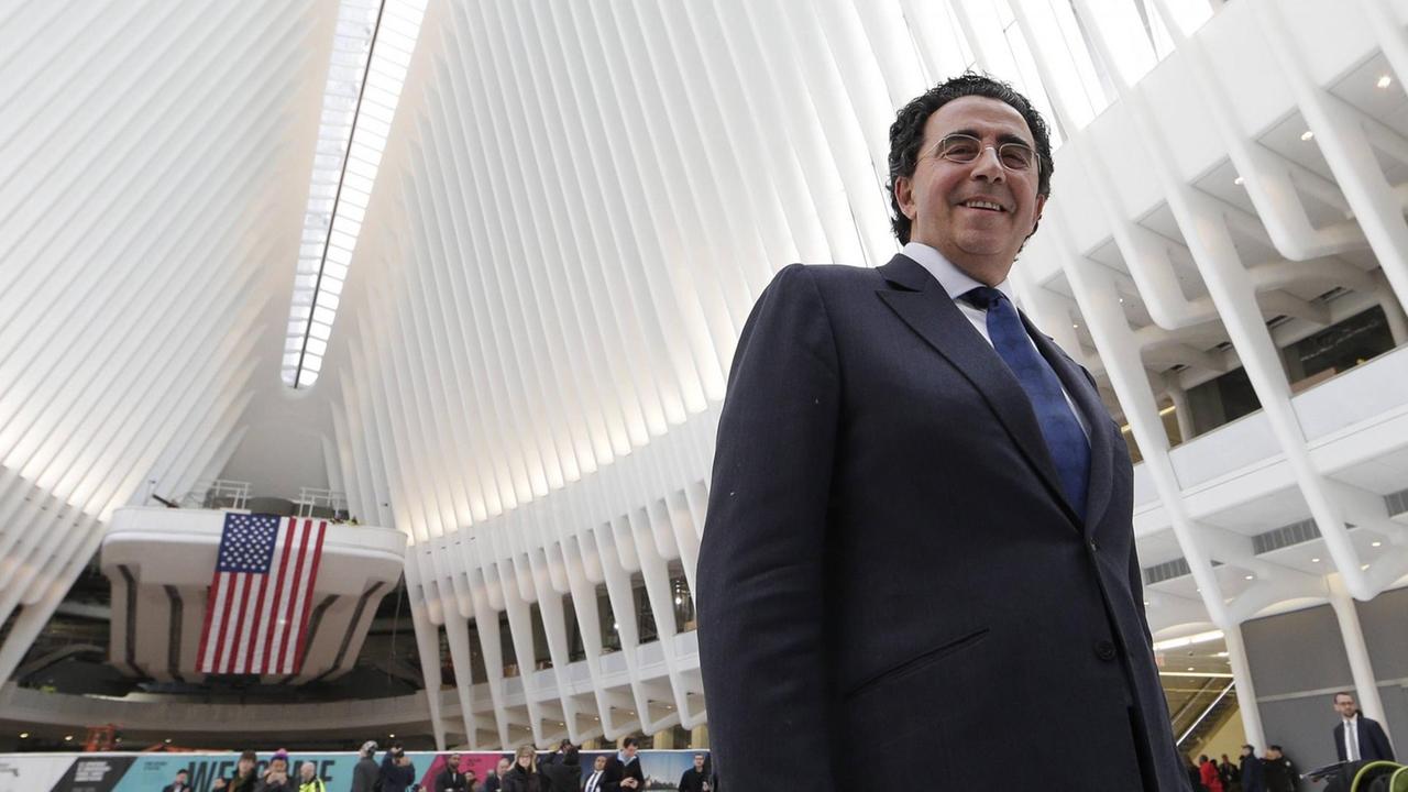 Der Architekt Santiago Calatrava lächelt in die Kamera, im Hintergrund ist der Innenraum des "Oculus"-Bahnhofs in New York zu sehen