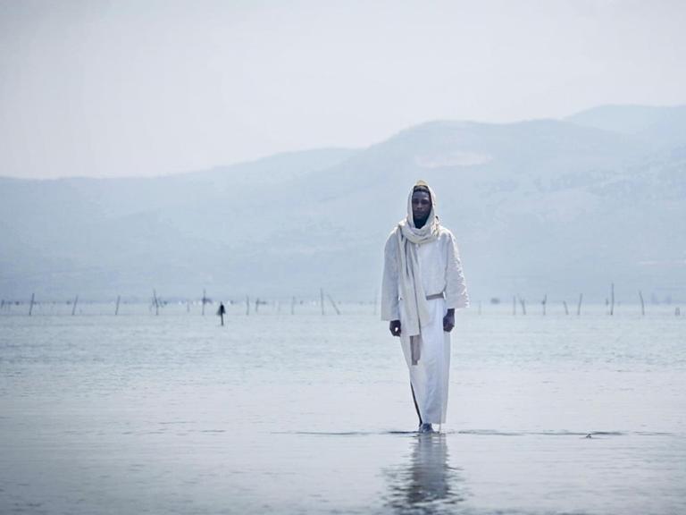 Eine Filmszene zeigt Yvan Sagnet der als schwarzer Jesus über das Wasser wandelt.