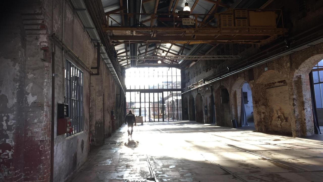 Eine leere Industriehalle mit Backstein Mauerwerk und großen Fenstern.