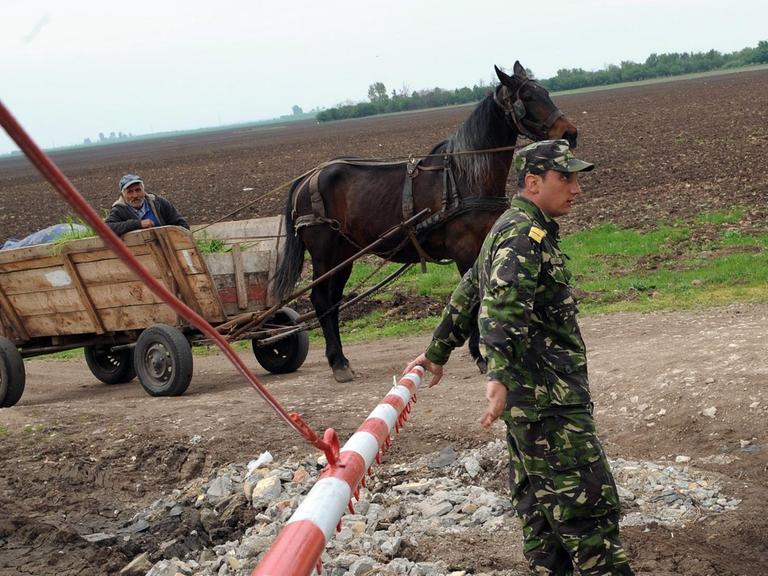 Ein rumänischer Soldat an einer Barriere nahe des militärischen Stützpunktes. Im Hintergrund ein Einwohner des Dorfes auf einem Pferdekarren.