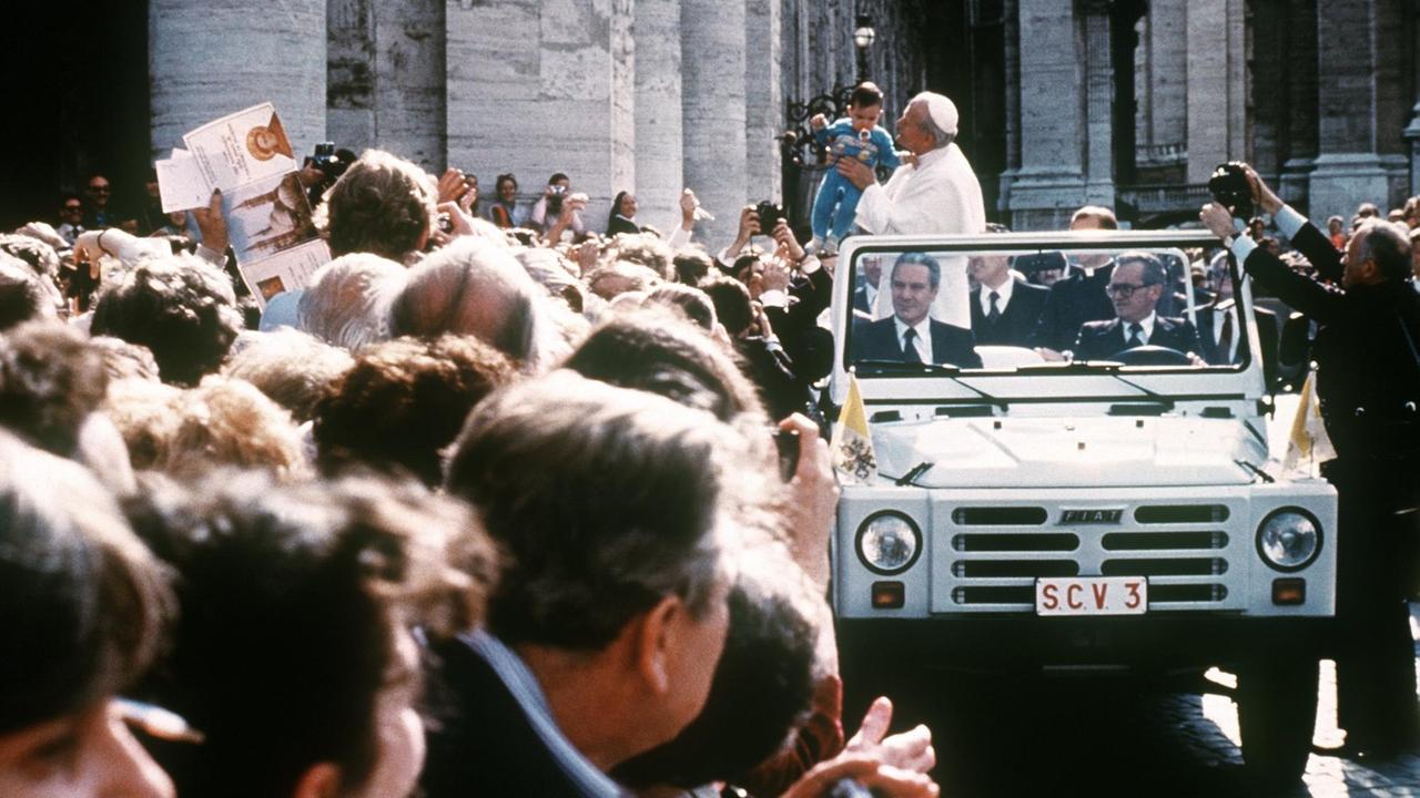 Papst Johannes Paul II. fährt am 13. Mai 1981 in einem offenen Fahrzeug an einer Menschenmenge auf dem Petersplatz in Vatikanstaat vorbei und hält ein kleines Kind auf dem Arm. Wenige Augenblicke später wurde er bei einem Attentat durch mehrere Schüsse schwer verletzt. Der Attentäter, der Türke Mehmet Ali Agca, konnte kurz Zeit danach verhaftet werden. (Bild: imago stock&people / ANSA)