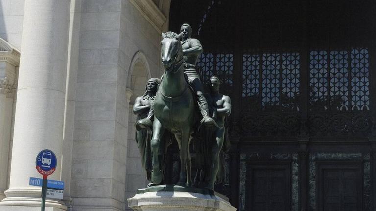 Die Statue des US-Präsidenten Theodore Roosevelt auf einem Pferd vor dem New Yorker Naturkundemuseum, neben ihm ein Indigener und ein Afrikaner Die Statue des US-Präsidenten Theodore Roosevelt auf einem Pferd vor dem New Yorker Naturkundemuseum, neben ihm ein Indigener und ein Afrikaner