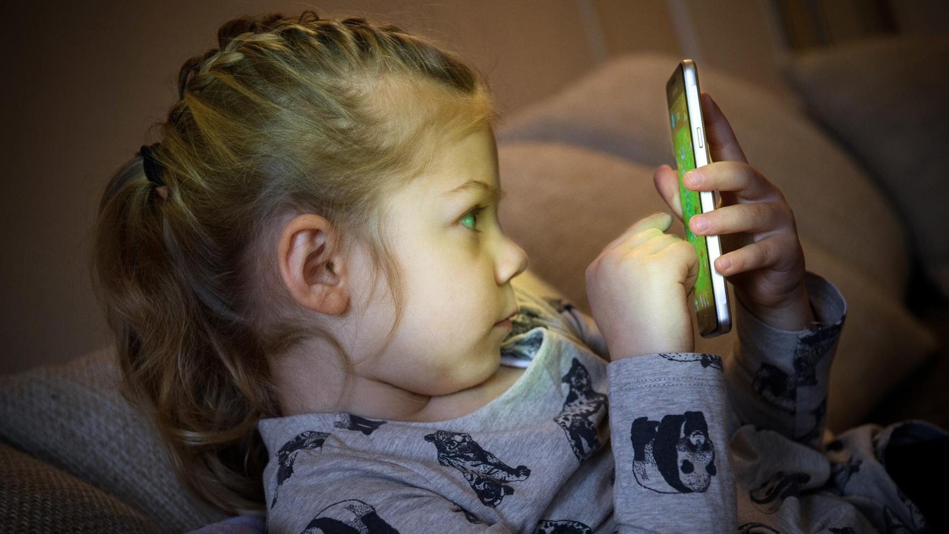  Ein kleines Mädchen spielt auf einem Smartphone.
