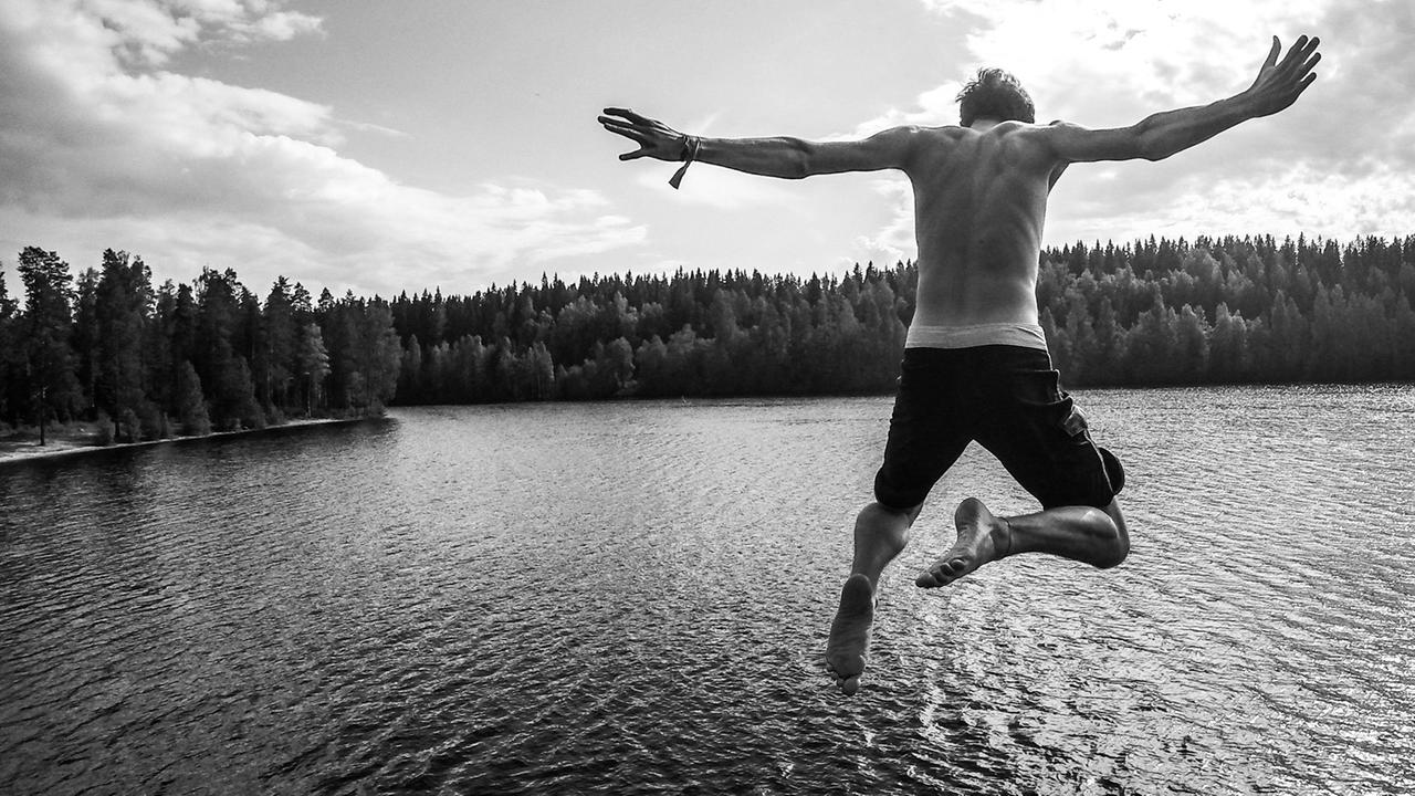 Ein junger Mann springt von einem Sprungturm in einen See.