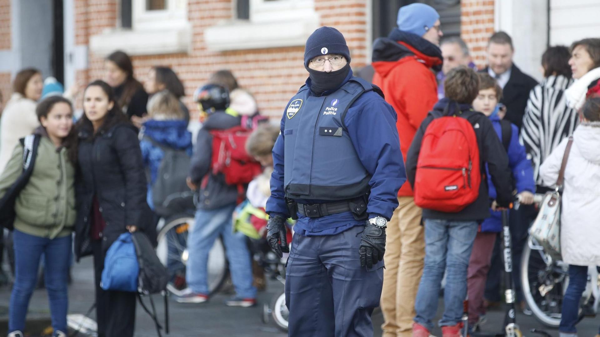 Man sieht einen Polizisten mit Mütze und kugelsicherer Weste, dahinter stehen Schüler.