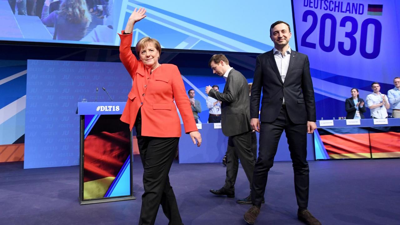 Merkel geht über die Bühne und hebt winkend den rechten Arm. Neben ihr Tobias Loose, Landesvorsitzender JU Schleswig-Holstein, und Paul Ziemiak, Bundesvorsitzender der Jungen Union Deutschland (JU).