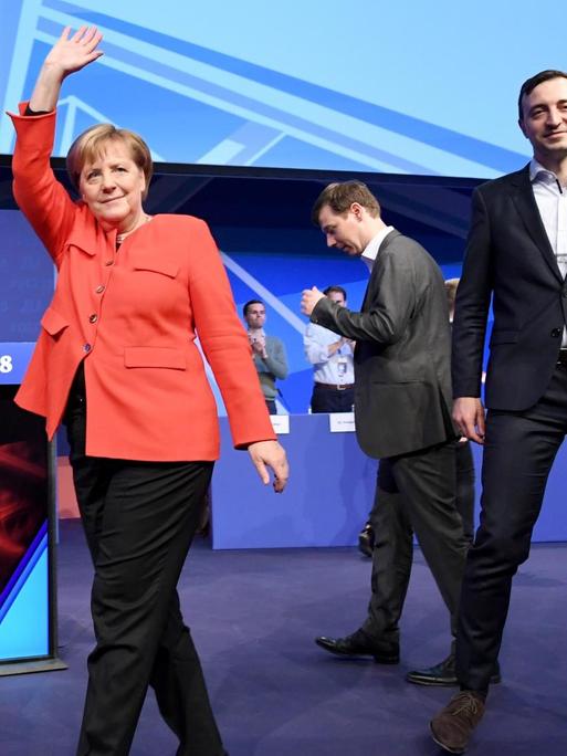 Merkel geht über die Bühne und hebt winkend den rechten Arm. Neben ihr Tobias Loose, Landesvorsitzender JU Schleswig-Holstein, und Paul Ziemiak, Bundesvorsitzender der Jungen Union Deutschland (JU).