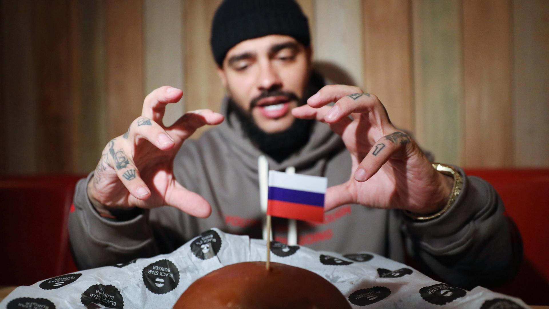Der Hip-Hop-Sänger Timati verkauft auf seinem Label nicht nur Musik, sondern auch Burger - hier sieht man ihn, wie er nach einem sogenannten "Präsidenten-Burger" mit kleiner Russland-Flagge greift, den es zum Putin-Geburtstag zum Verkauf gab
