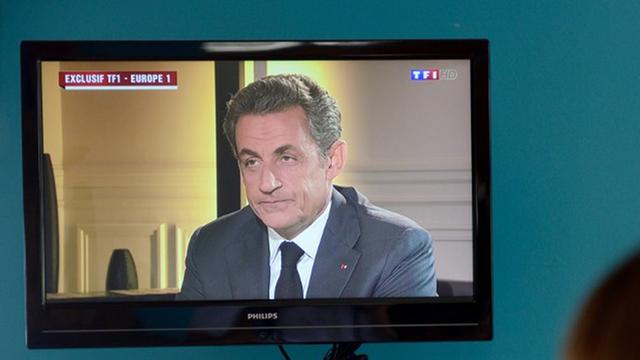 Eine Frau beobachtet ein Fernsehinterview mit dem ehemaligen französischen Präsidenten Nicolas Sarkozy, der sich mit Korruptionsvorwürfen konfrontiert sieht.