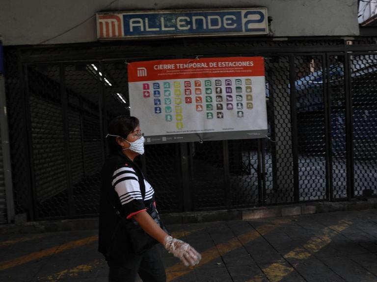 Eine Frau mit Maske und Handschuhen läuft an einer geschlossenen Metro-Station in Mexiko-Stadt vorbei.