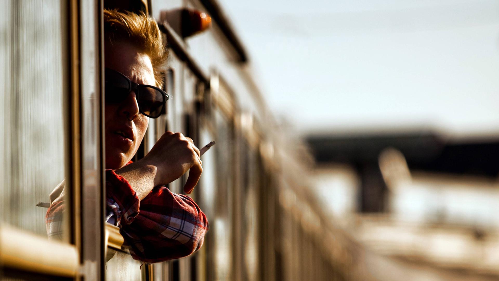 Ein junger Mann mit Zigarette schaut aus einem Zugfenster