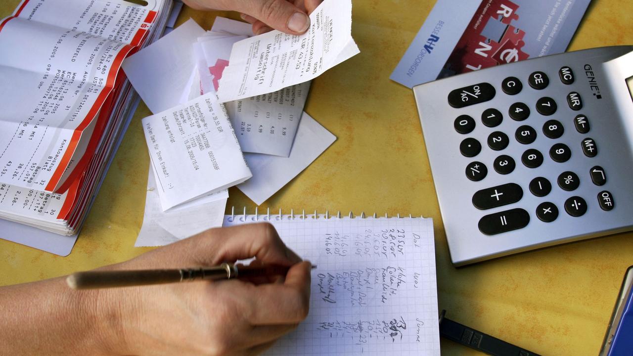 Diverse Quittungen und Rechnungen werden mit dem Taschenrechner zusammengezählt und in ein Haushaltsbuch eingetragen.