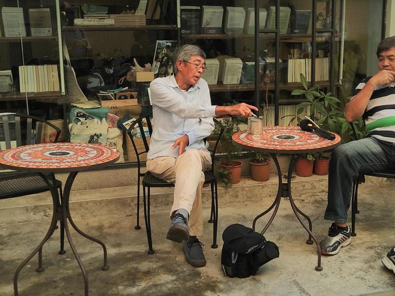 Buchhändler Lam Wing-kee vor einem Bücher-Café in seiner neuen Heimat Taiwan. Er raucht und spricht mit Journalisten.