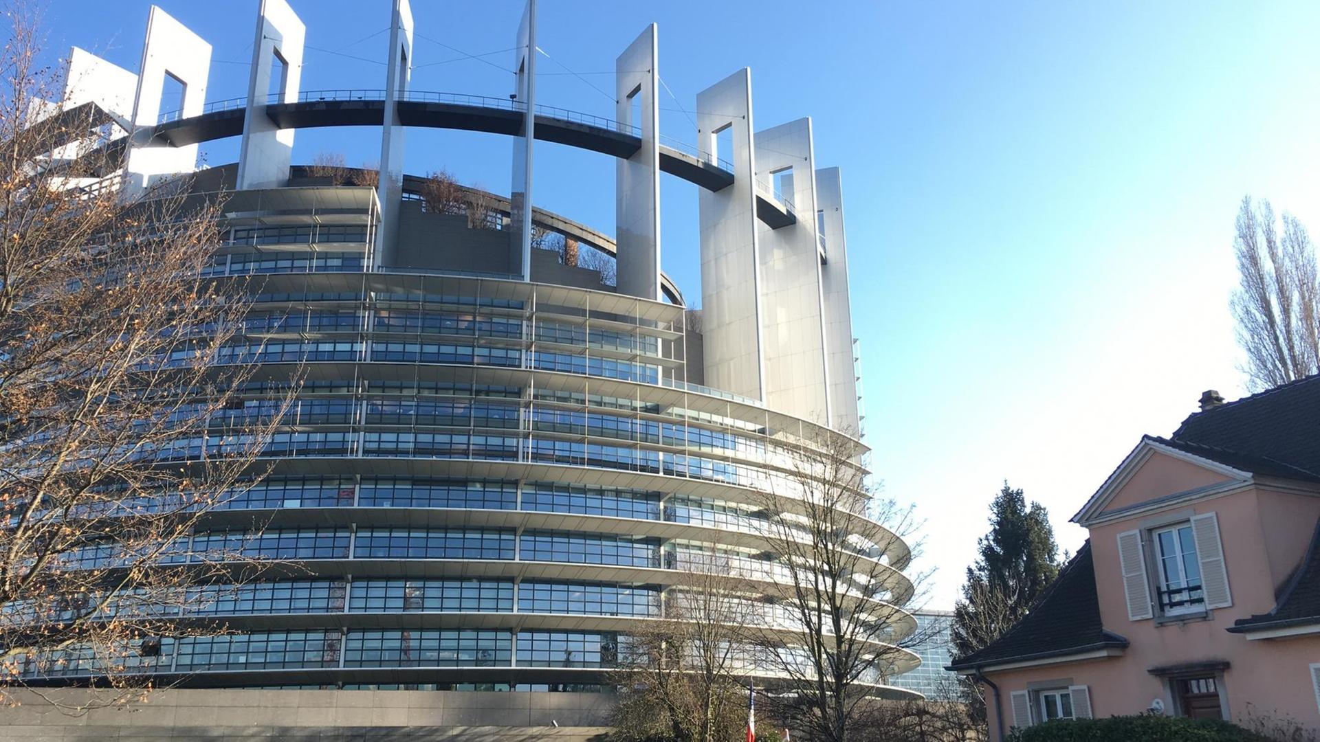 Das Europäische Parlament in Straßburg vor blauem Himmel, rechts daneben ein angrenzendes Wohnhaus.