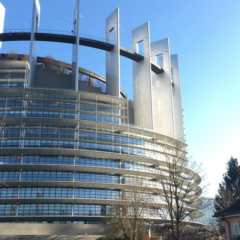 Das Europäische Parlament in Straßburg vor blauem Himmel, rechts daneben ein angrenzendes Wohnhaus.