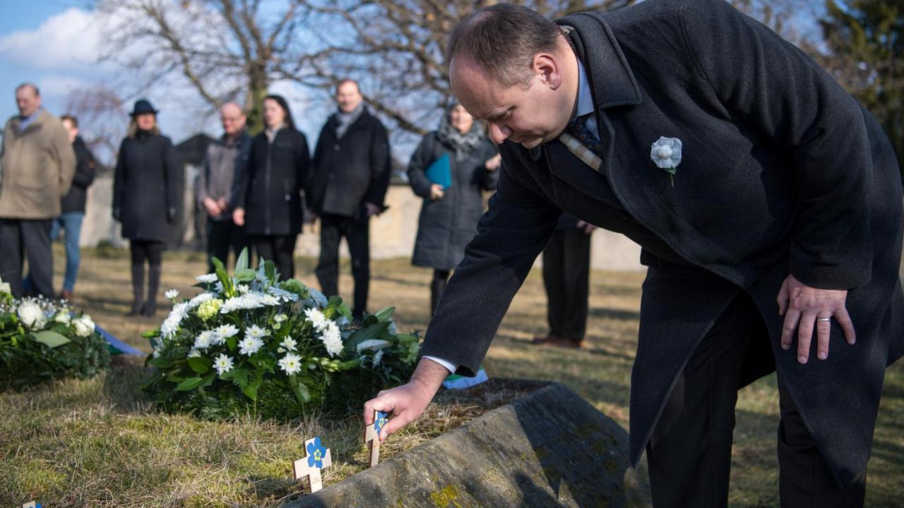Dresdens Oberbürgermeister Dirk Hilbert steckt während einer Gedenkveranstaltung auf dem Alten Annenfriedhof ein kleines Holzkreuz in die Erde vor einer Gedenkstele.