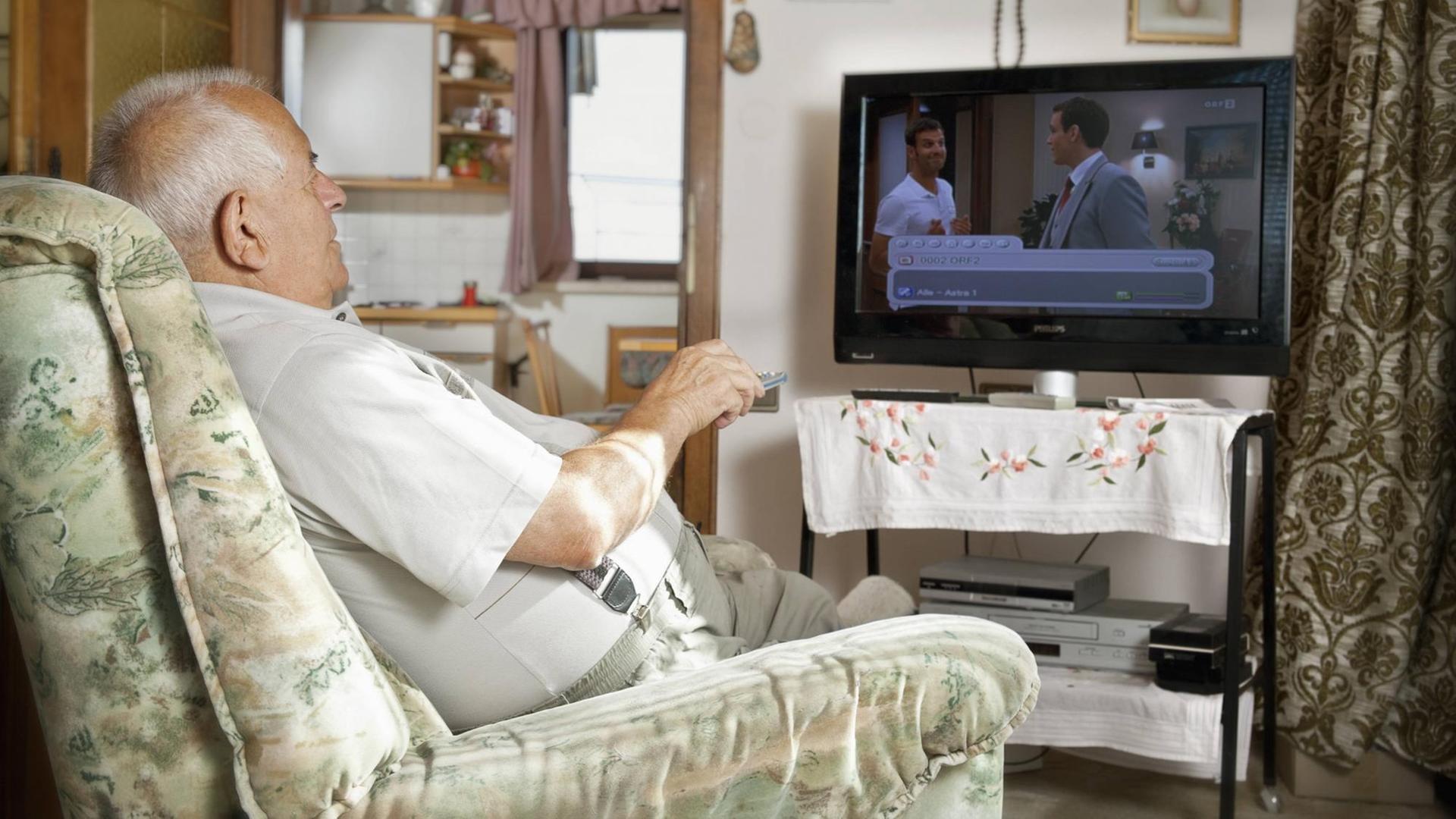 Ein älterer Mann sitzt vor dem Fernseher.
