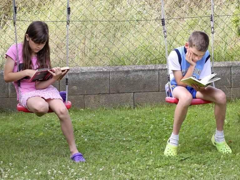 Ein Mädchen und ein Junge lesen Bücher und sitzen dabei auf Schaukeln