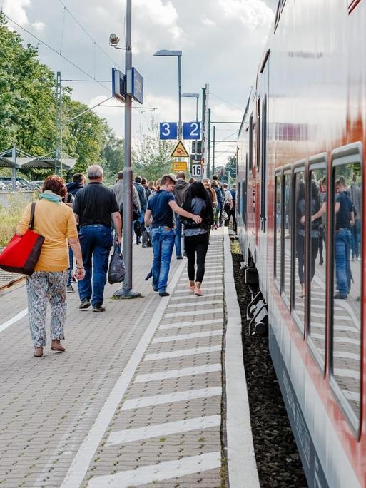 Bahnkunden gehen auf dem Bahnsteig an einem Regionalexpress der Deutschen Bahn (DB) entlang.