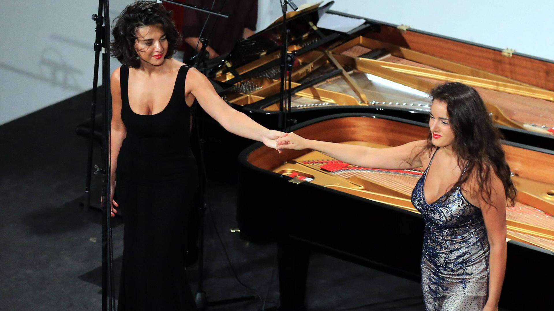 Die georgischen Pianistinnen Khatia (l.) und Gvantsa Buniatishvili stehen Hand in Hand vor einem Flügel nach ihrem Auftritt am Rheingau Musik-Festival auf Schloss Johannisberg in Geisenheim