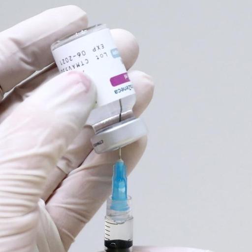 Medizinisches Personal hält eine Spritze mit dem Imfpstoff von Astrazeneca in den Händen. Spritze und Ampulle sind halb verdeckt. Die Person trägt weiße Latexhandschuhe.