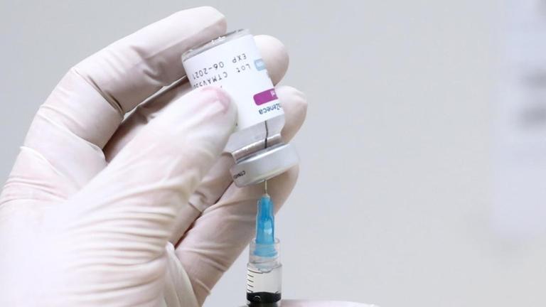 Medizinisches Personal hält eine Spritze mit Imfpstoff in den Händen. Spritze und Ampulle sind halb verdeckt. Die Person trägt weiße Latexhandschuhe.