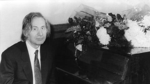 Der russische Komponist und Pianist Alfred Schnittke, schwarz-weiß-Aufnahme, an einem Klavier sitzend, in die Kamera blickend.