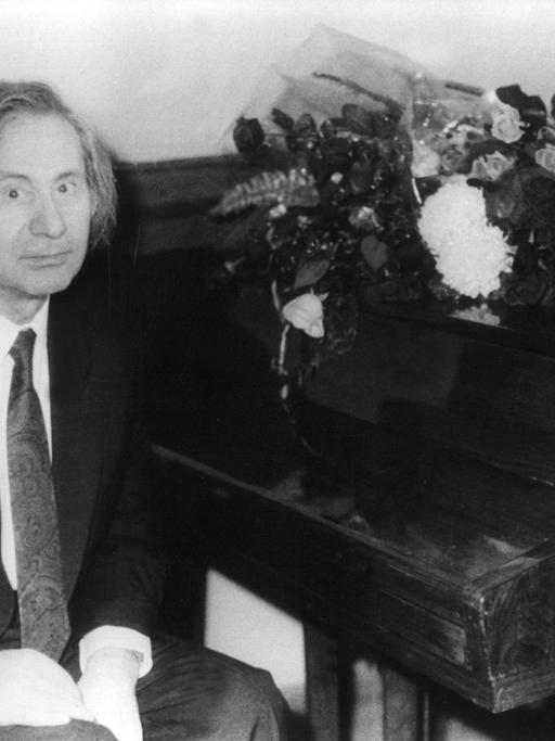 Der russische Komponist und Pianist Alfred Schnittke, schwarz-weiß-Aufnahme, an einem Klavier sitzend, in die Kamera blickend.