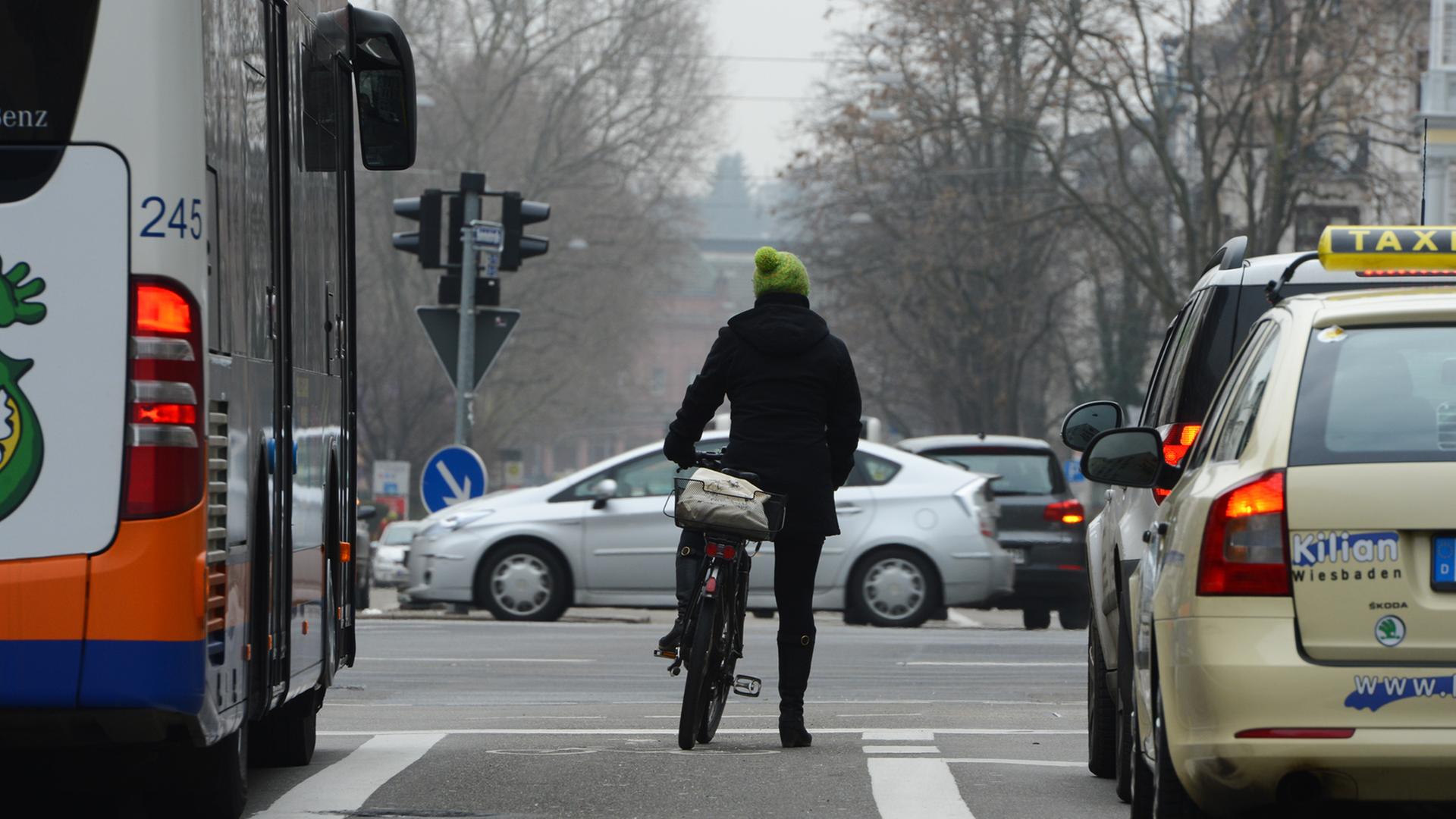 Eine Frau steht am 18.02.2015 in Wiesbaden (Hessen) mit ihrem Fahrrad an einer belebten Kreuzung.