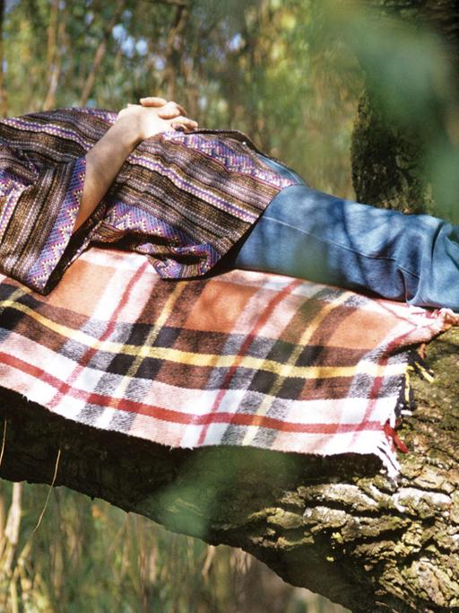 Ein Mann liegt schlafend auf dem Ast eines Baumes.