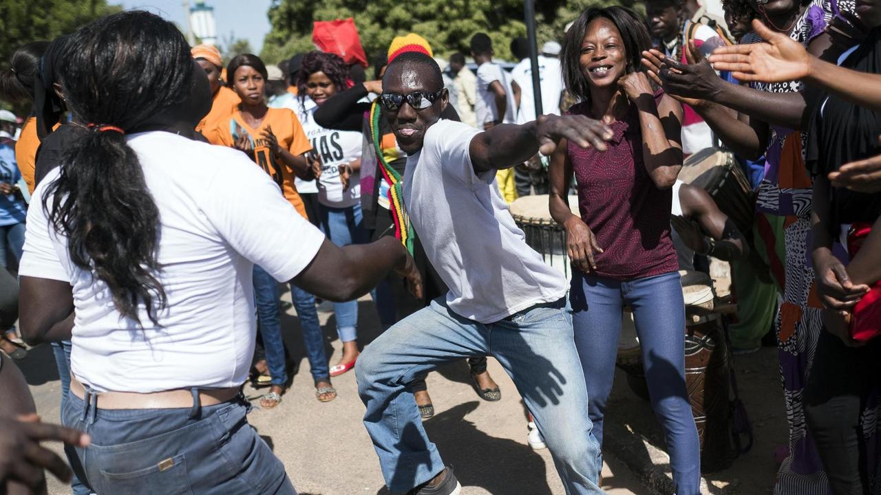 Jugendliche Anhänger von Adama Barrow tanzen auf der Straße.