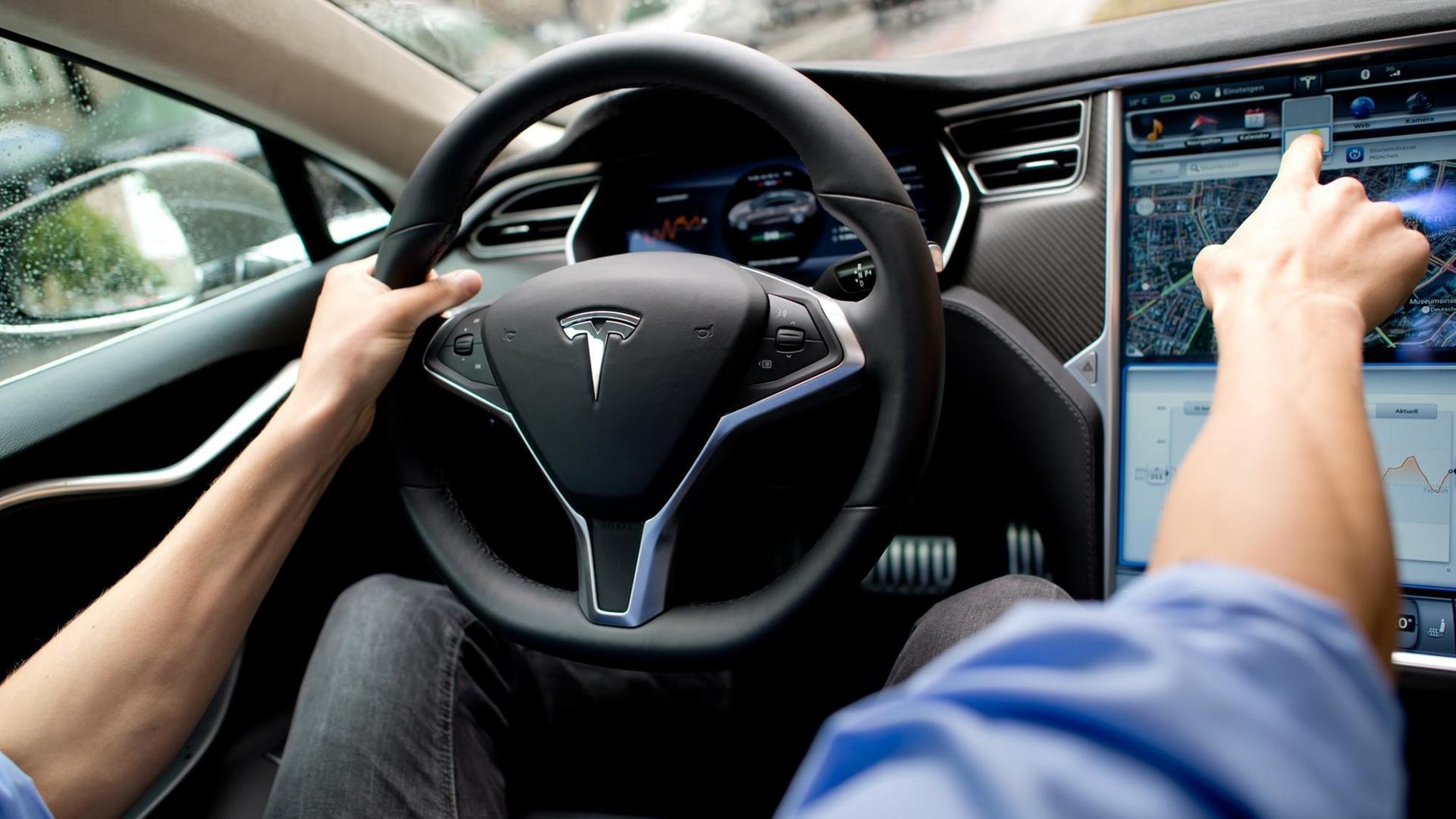 Ein Mann sitzt in einem Tesla Model S auf dem Fahrersitz vor einem Showroom des Autoherstellers.