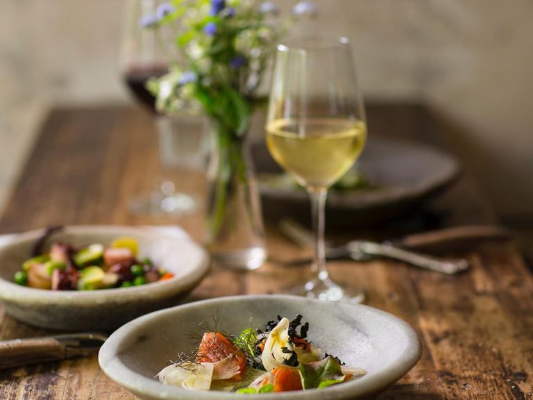 Auf einem Tisch stehen Schüsseln mit Salat, Weingläser und ein Vase mit Blumen.