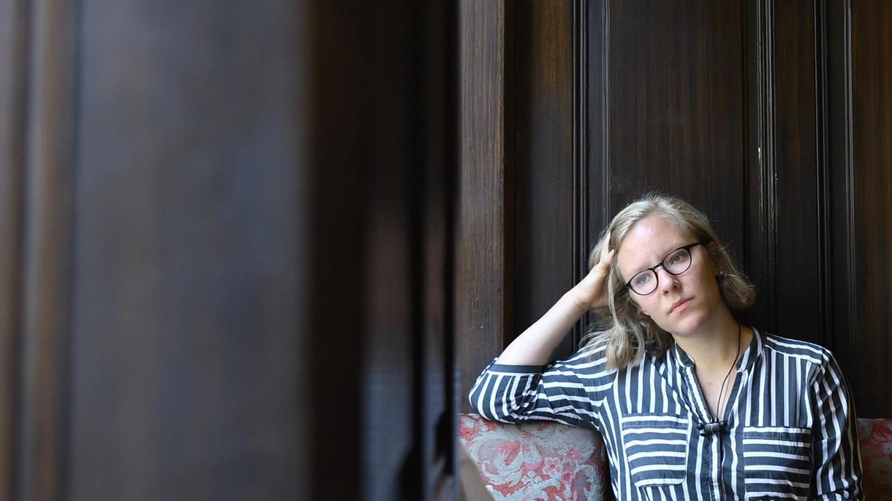 Das Bild zeigt die die österreichische Schriftstellerin Raphaela Edelbauer, die vor einer dunklen Holzwand sitzt.