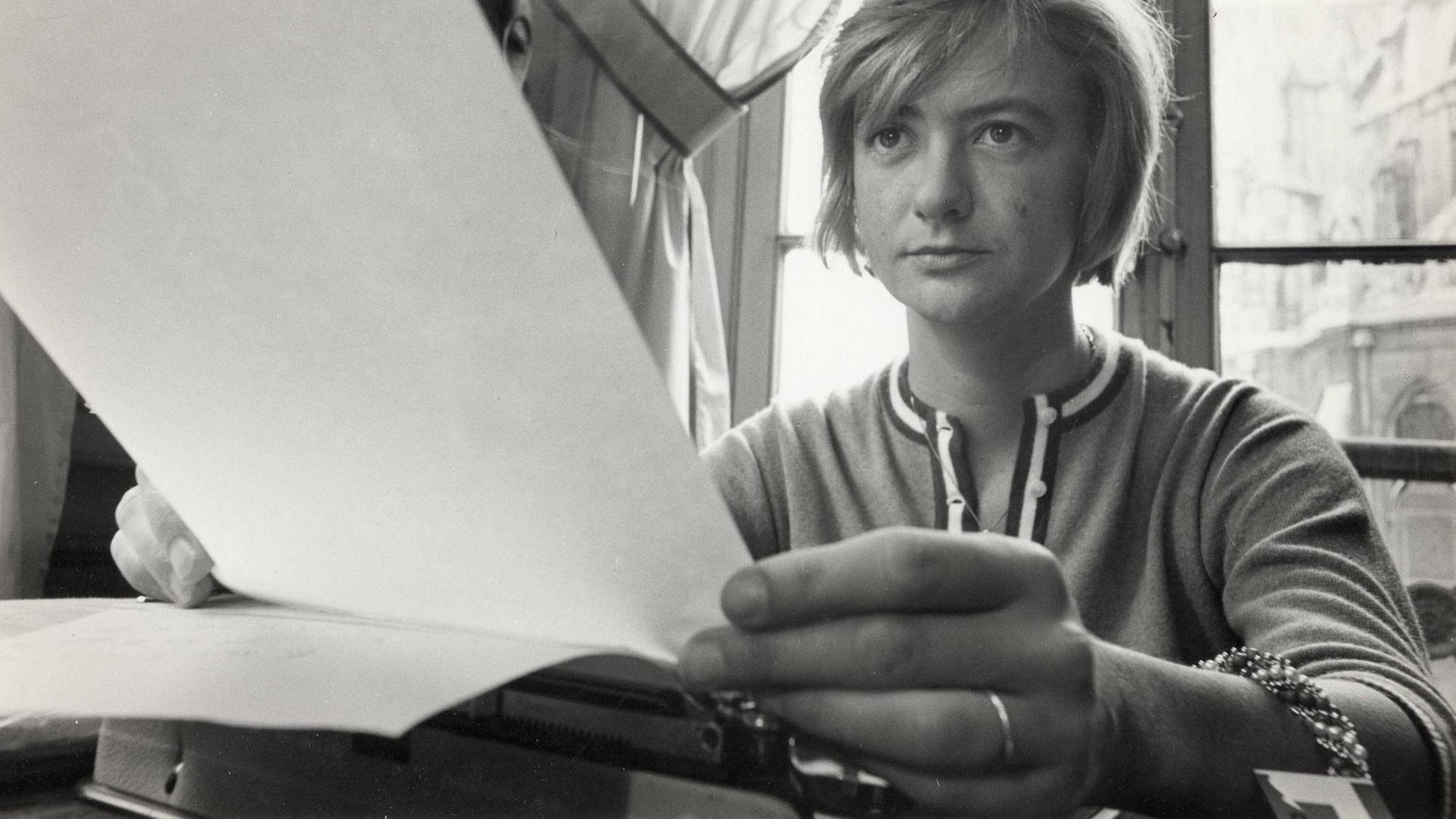 Françoise Sagan sitzt an ihrer Schreibmaschine und hält Blätter in der Hand.