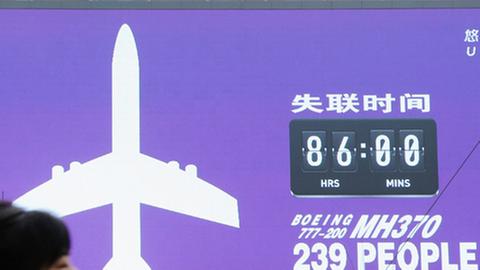 Eine Frau passiert eine Anzeigetafel in Peking, die die Stunden seit dem Verschwinden des malaysischen Flugzeugs zählt.