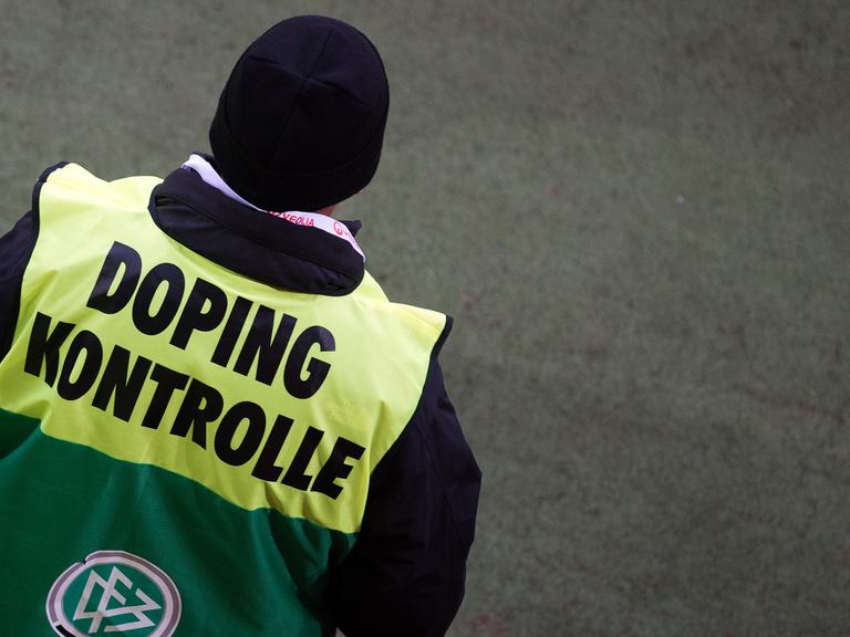 Ein Dopingkontrolleur von hinten mit gelb-grüner Jacke und der Aufschrift "Dopingkontrolle".