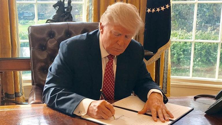 Trump unterschreibt am Schreibtisch sitzend im Oval Office