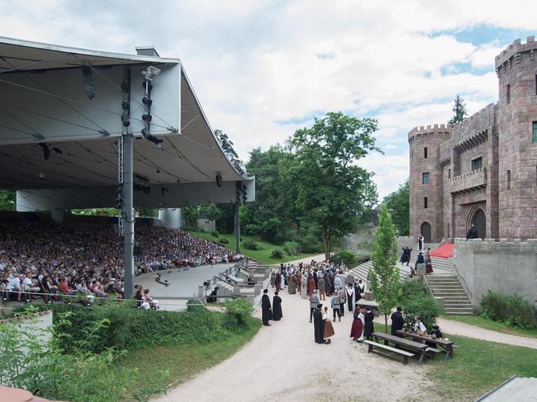 Panorama einer großen Freilichtbühne mit einem großen, überdachten Zuschauerraum und einer Burg, die den Schauspielern als Kulisse dient.