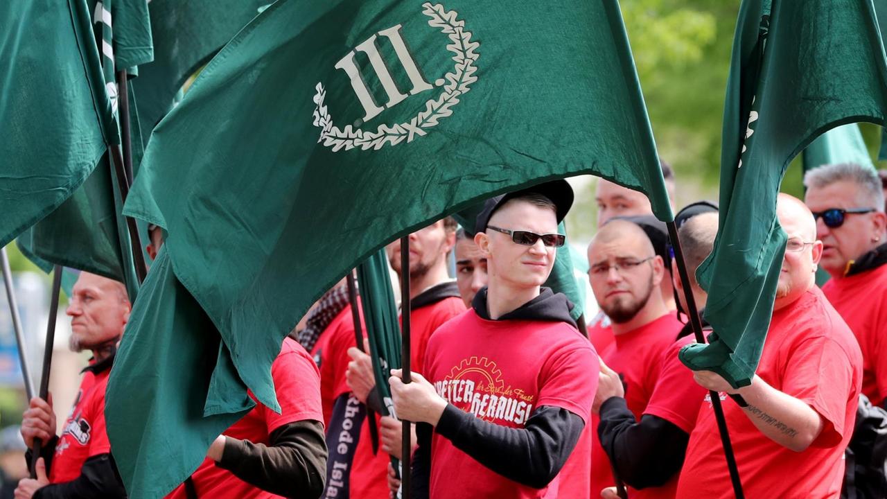 Mehrere Demonstranten in bedruckten roten T-Shirts tragen die grünen Fahnen des "III.Weg"