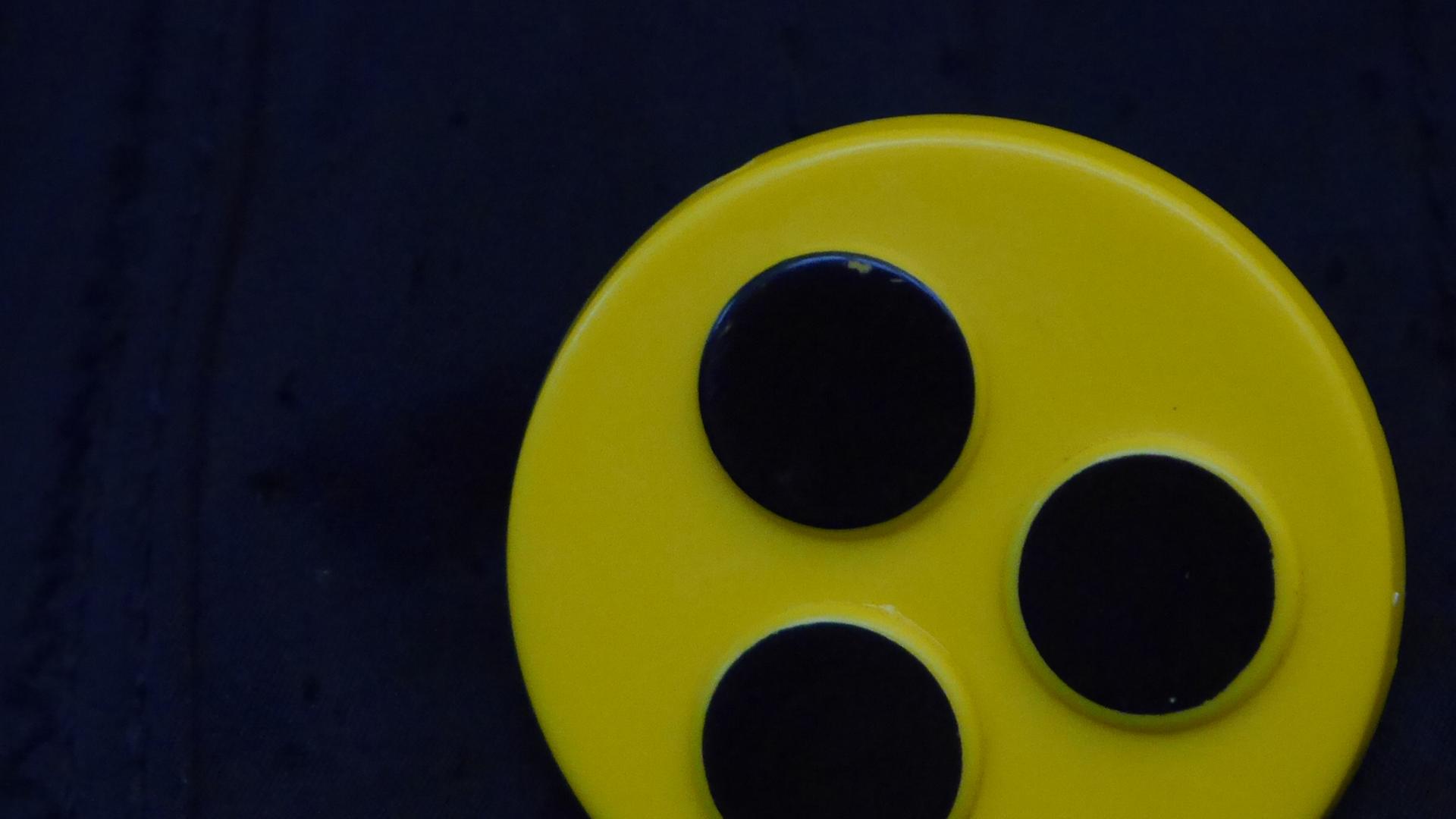 Ein Blindenbutton: Drei schwarze Punkte auf gelbem Kreis.