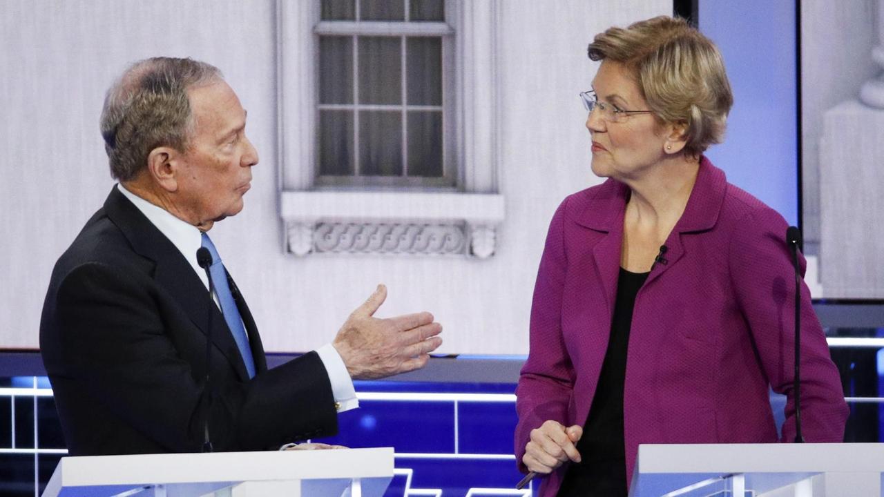 Die beiden sind einander zugeneigt. Bloomberg spricht zu Warren und gestikuliert mit der rechten Hand. 