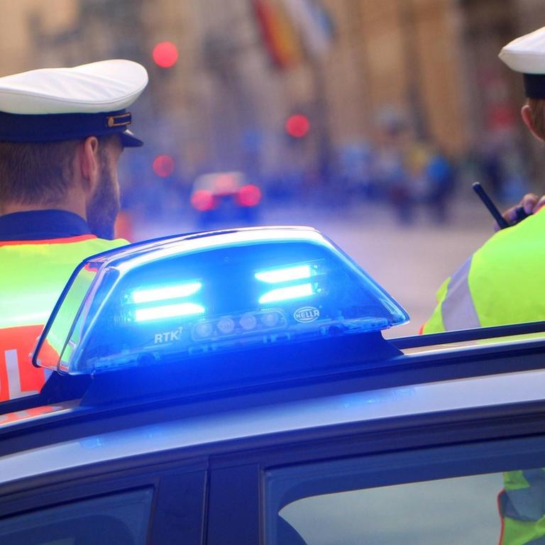 Polizisten stehen neben einem Einsatzwagen der Polizei mit eingeschaltetem Blaulicht